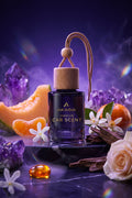 A bottle of Avasia Premium Car Scent displayed in a styled setting with purple crystals, orange slices, white flowers, cinnamon sticks, and a rose on a dark reflective surface.